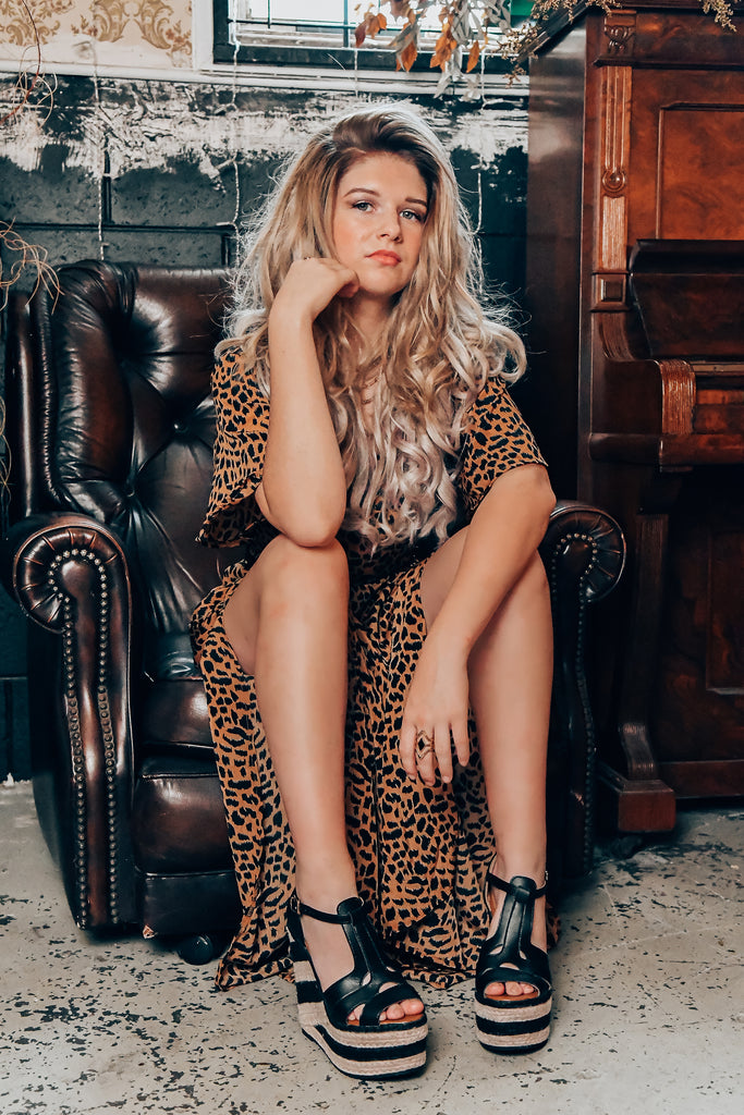 Lady sitting on a vintage couch wearing a leopard print dress and black striped platform wedge shoes